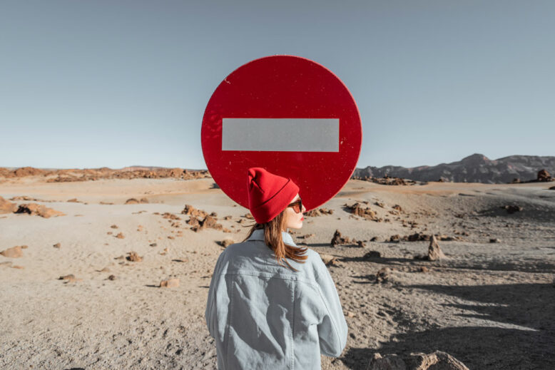 woman dressed in jeans and red hat traveling on the dessert valley. standing near the traffic sign on the roadside