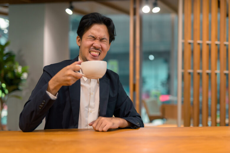 Businessman sitting at a restaurant and being disgusted by his hot drink.