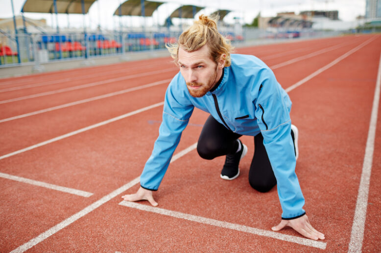 Young determined man in sportswear standing by start line on race track