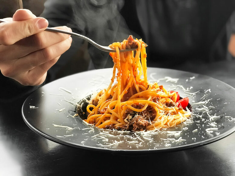 Italian pasta with meat, cheese and cherry tomatoes in black plate on black wooden table background