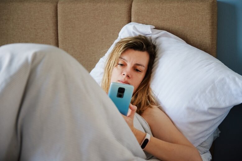 Bored woman looking at her phone in bed.