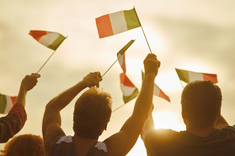 Young people waving italian flags, back view. Italian family against evening sky background.