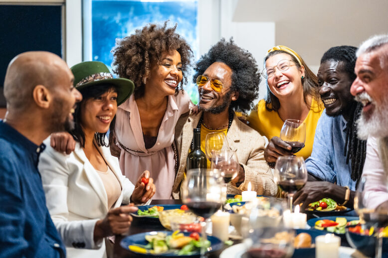 Different people of age and ethnicity eating a vegan dinner. Multiethnic group of friends having fun while sharing a meal in a warm and welcoming house.