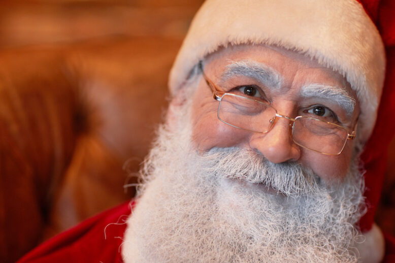 Portrait of smiling kind senior Santa Claus with white beard and eyebrows wearing eyeglasses and cap