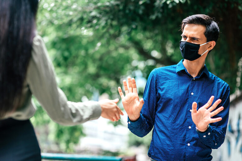 stop. Young man in mask standing outdoors refusing to shake hands with his friend, woman to protect himself from coronavirus. Social distancing, no connection concept. Focus on people.Horizontal shot