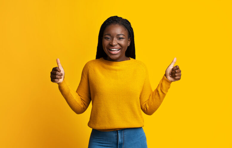 Joyful African American Woman In Bright Sweater Showing Thumbs Up At Camera