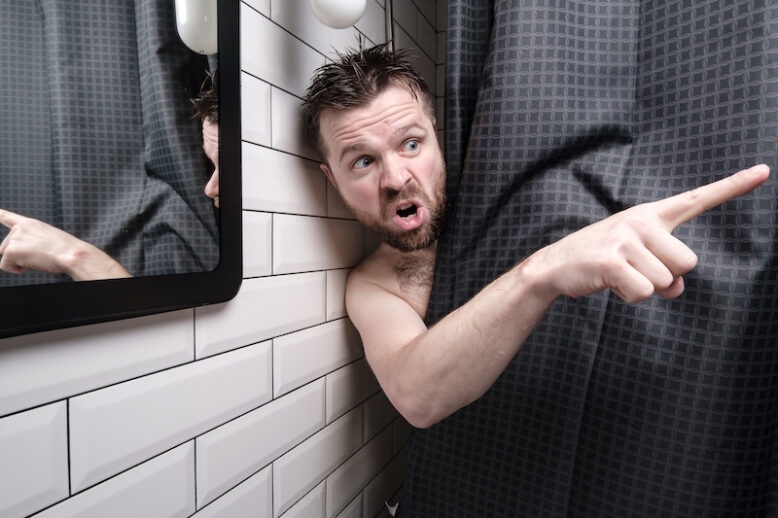 Caucasian man is furious, peeking out from behind a shower curtain