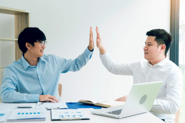 Two businessmen high five as they agree on the company's budget.