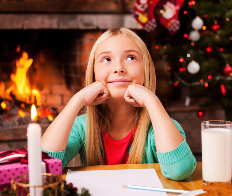Cute little girl day dreaming while sitting at home with Christmas tree and fireplace in the background