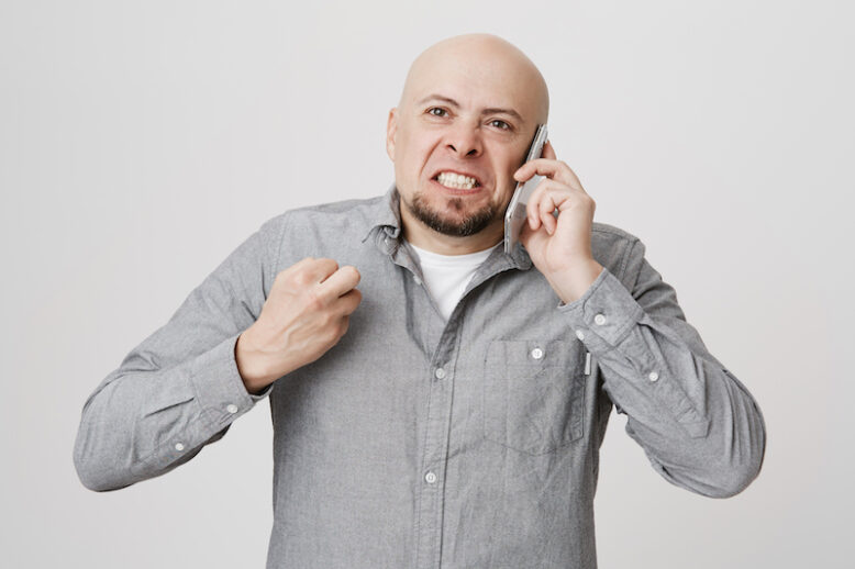 Portrait of mad bald guy swearing while talking on smartphone