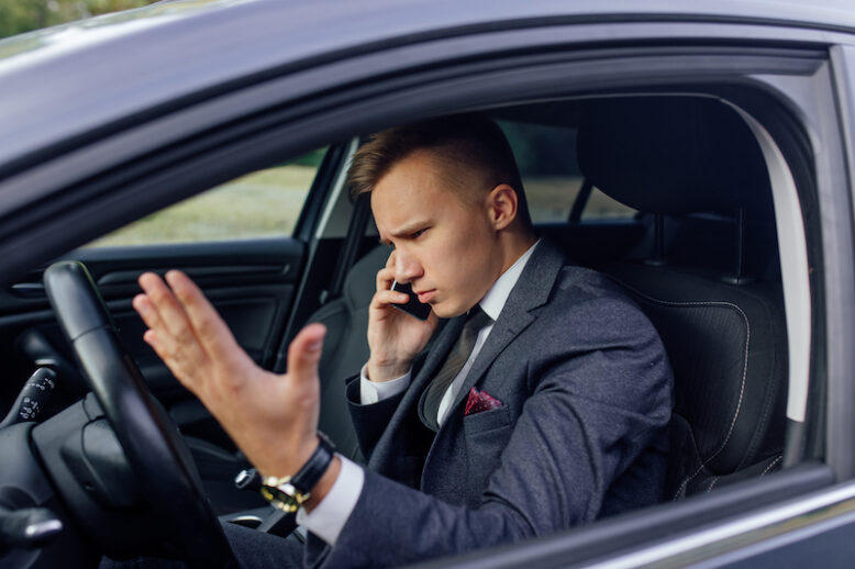 Stressed businessman swearing and talking phone while sitting inside car indoors.