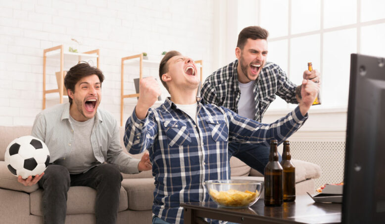 Excited friends watching football and cheering for favourite team at home