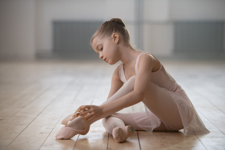 Little ballerina sitting on the floor and preparing for the classes in dance studio