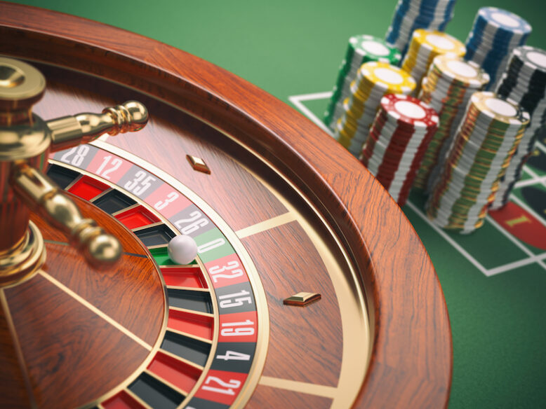 Casino roulette wheel with casino chips on green table.