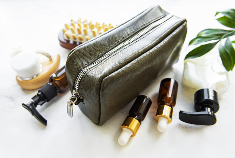 Green leather cosmetic bag and natural cosmetics on white marble background