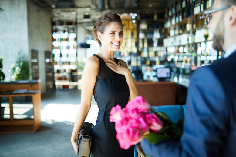 Cheerful young woman expressing gladness while looking at her boyfriend with rose bouquet