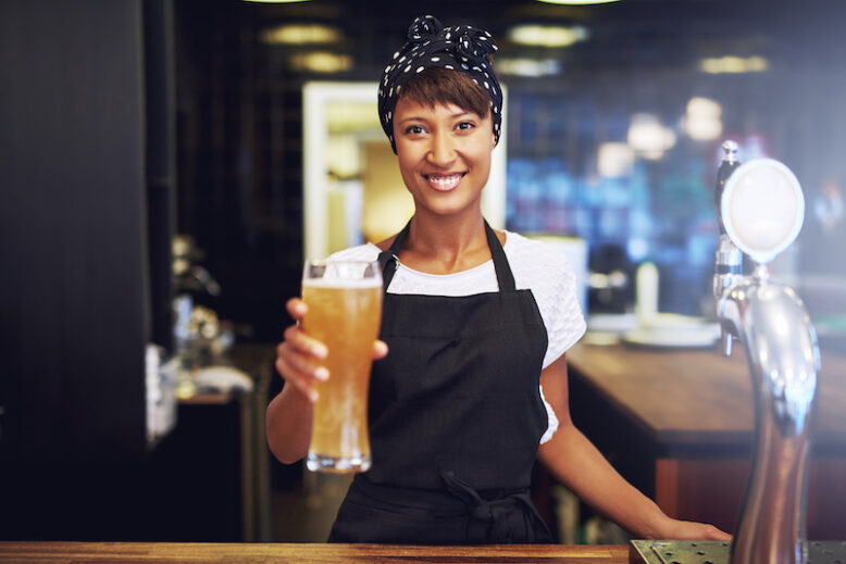 Smiling friendly waitress serving a pint of draft beer in a pub.