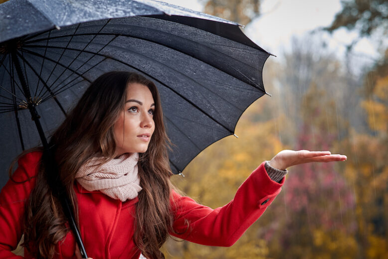 Young woman with black umbrella in the rain on an autumn cold day.