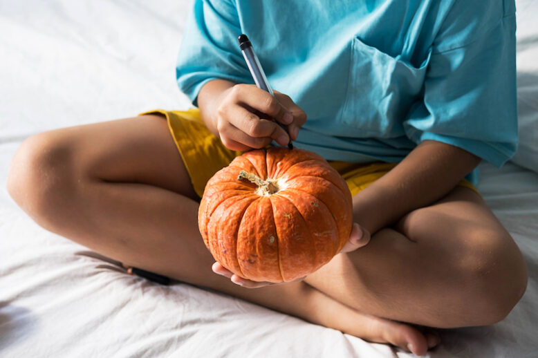 little boy drawing on pumpkin