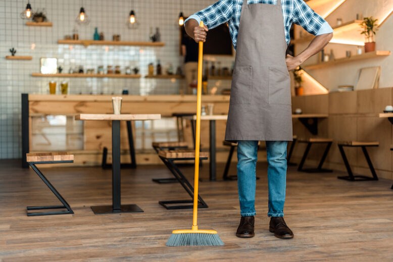 cropped view of a worker standing with broom in coffee shop