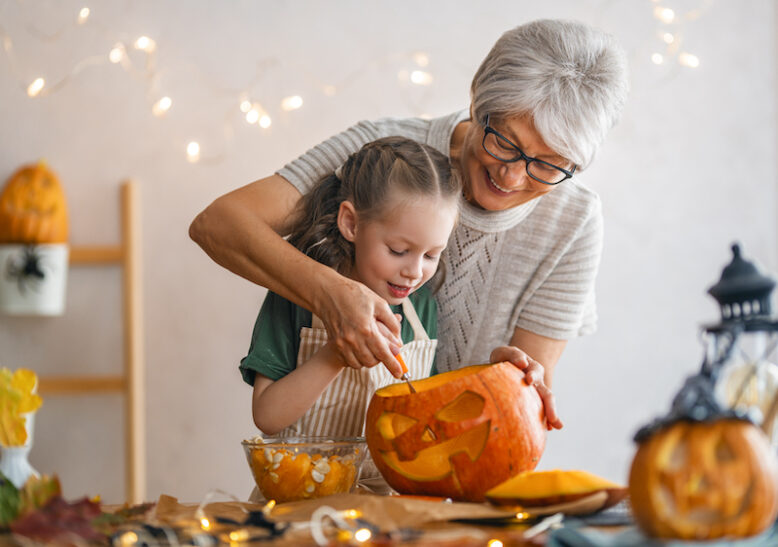 Happy family preparing for Halloween. Grandmother and granddaughter carving pumpkins at home.