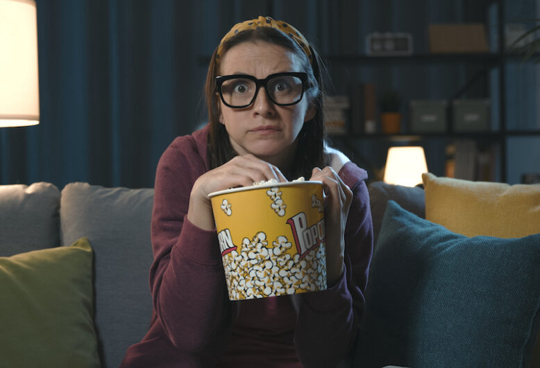 Woman watching a scary movie at home alone and eating popcorn