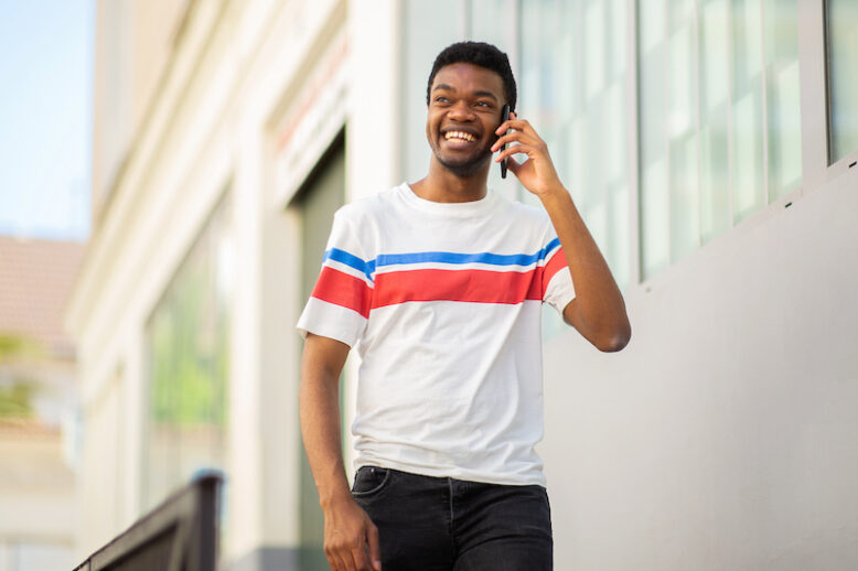 Portrait young African American man walking and talking with cellphone in city