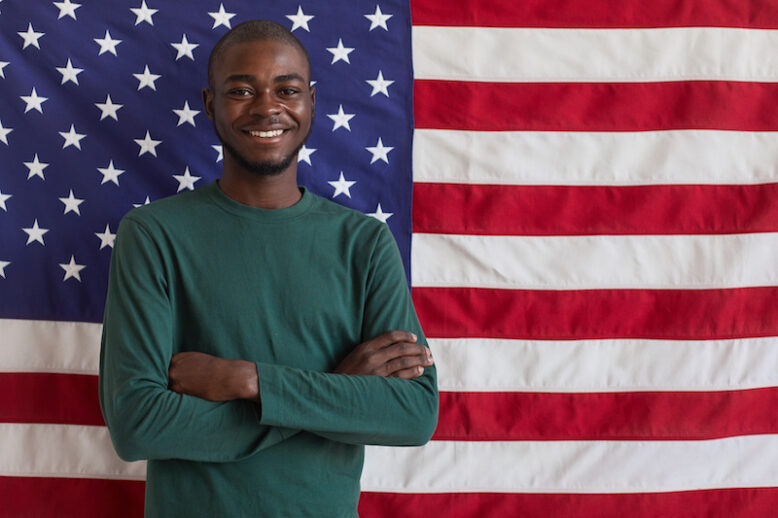 Portrait of young Afro-American man standing with arms crossed and smiling at camera against the American flag