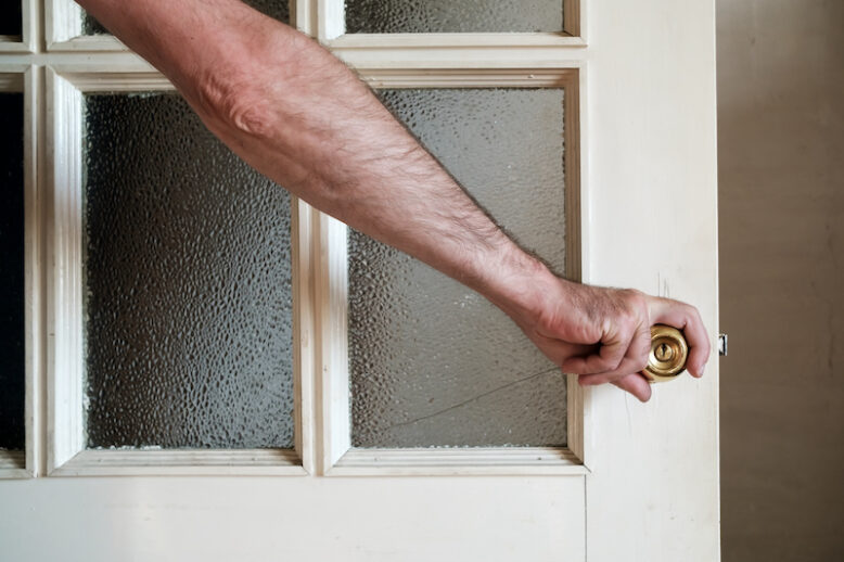 Male hand closes a white painted wooden door with frosted glass in a country house. Close-up.