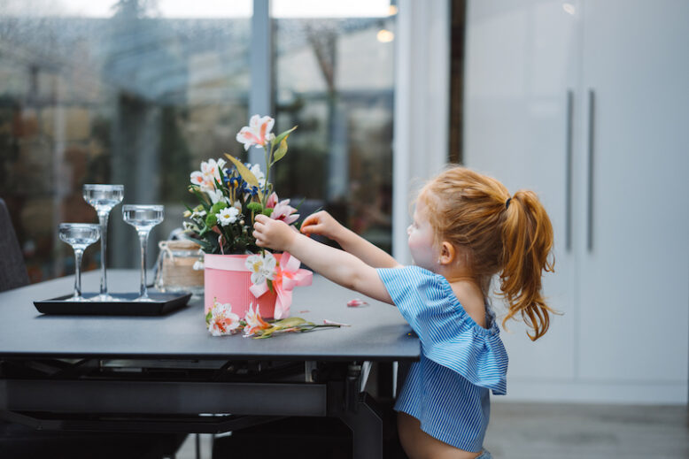 Little girl puts flowers on table, indoor