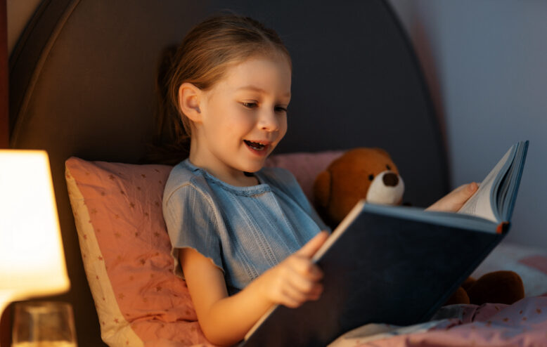 Cute little girl is reading a book in her bedroom.
