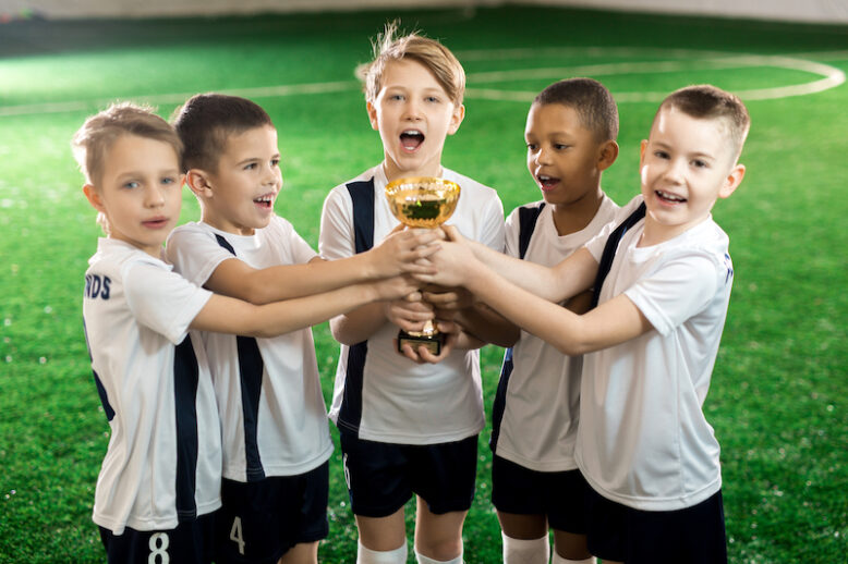 Team of little winners showing golden award after successful game in football championship