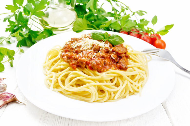 Spaghetti pasta with Bolognese sauce of minced meat, tomato juice, garlic, wine and spices with cheese and fork in a plate, vegetable oil, spicy herb on a light wooden board background