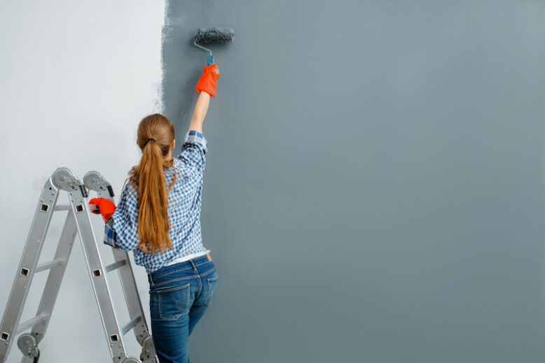 Female house painter paints walls indoors. 
