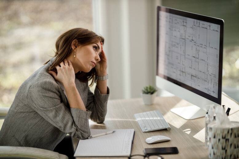 Business woman looking overly stressed while working on computer in her office.