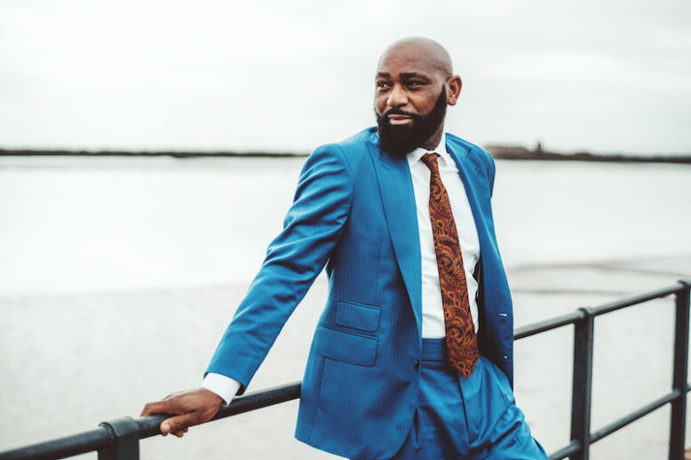 Handsome muscular bald mature black man with beard wearing elegant blue outfit and tie