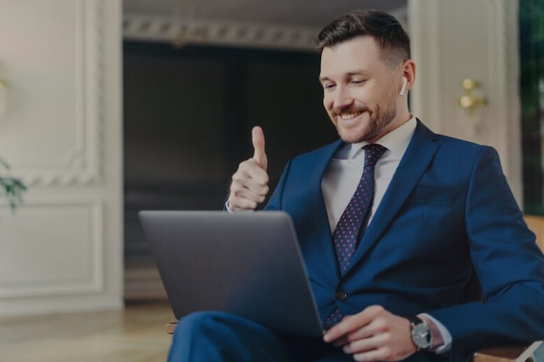 Happy attractive business professional in elegant suit showing his satisfaction by gesture thumb up during video conference.