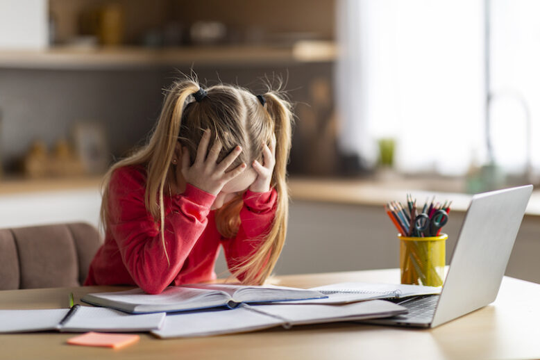 Dyslexia concept.Little girl working hard on homework, stressed preteen girl with dyslexia, sitting at table at home, looking at book and touching head in despair, copy space