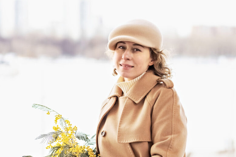 Portrait of a young woman in a beige coat and hat with a bouquet of mimosa in her hands. 