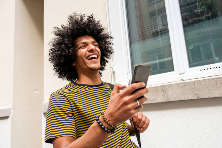 Close up portrait laughing young man walking with cellphone in city