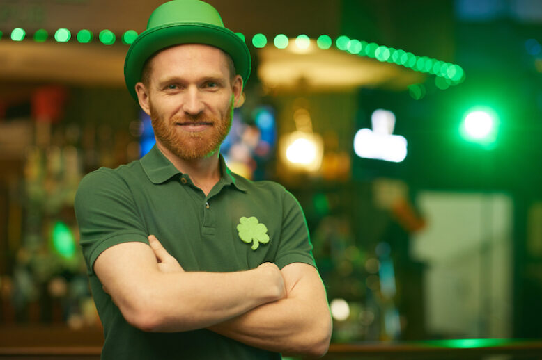 Portrait of young man in green hat standing with his arms crossed and smiling at camera in the pub