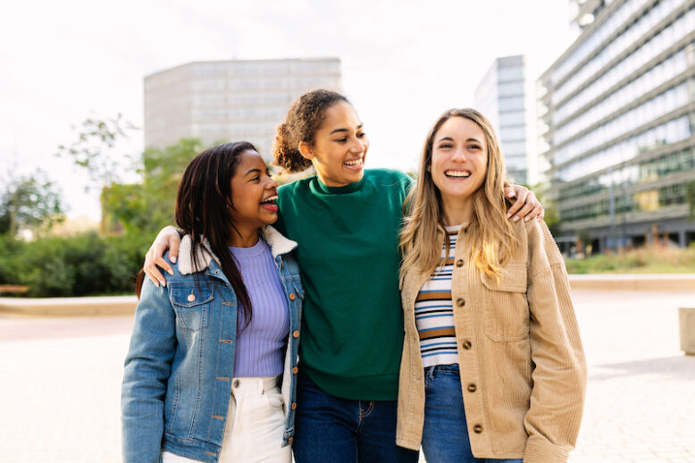 Three happy multiracial young women laughing outdoors. United female best friends having fun walking on city streets.Community and international friendship concept