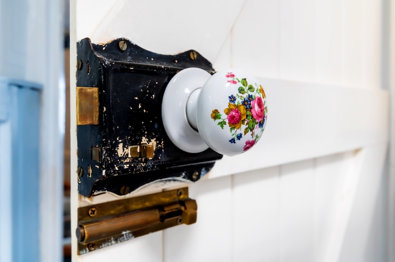 Close-up at Victorian style round porcelain floral decorated door knob on white wooden barn style door.