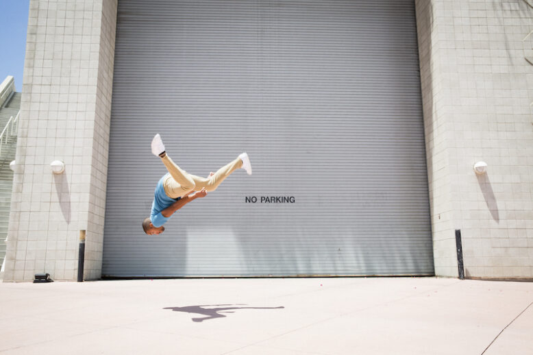 Young man somersaulting in front of a garage door.
