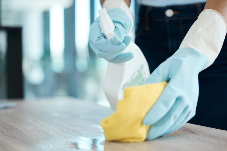 Hands with gloves cleaning a surface with spray