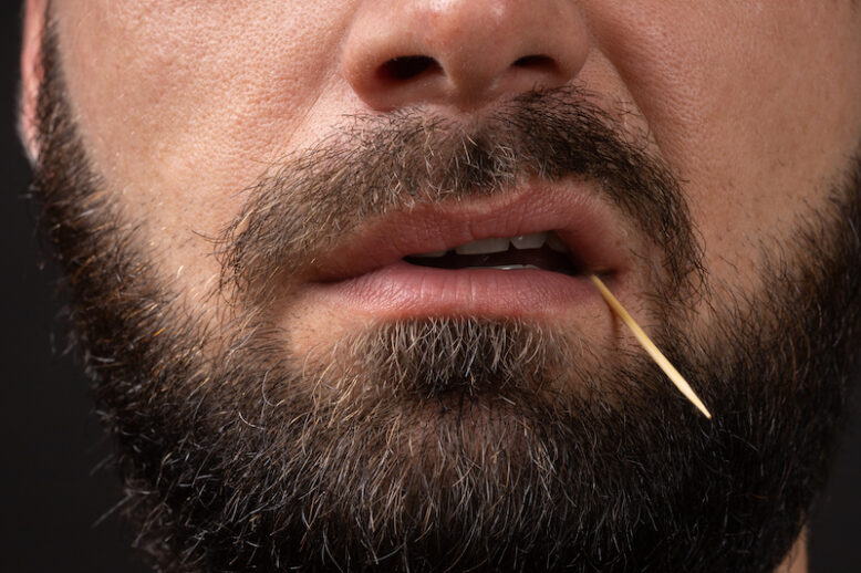 bearded face of a man with toothpick in teeth