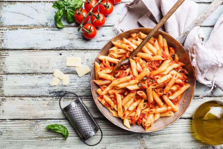 Penne pasta in tomato sauce and cheese decorated with basil on a wooden background