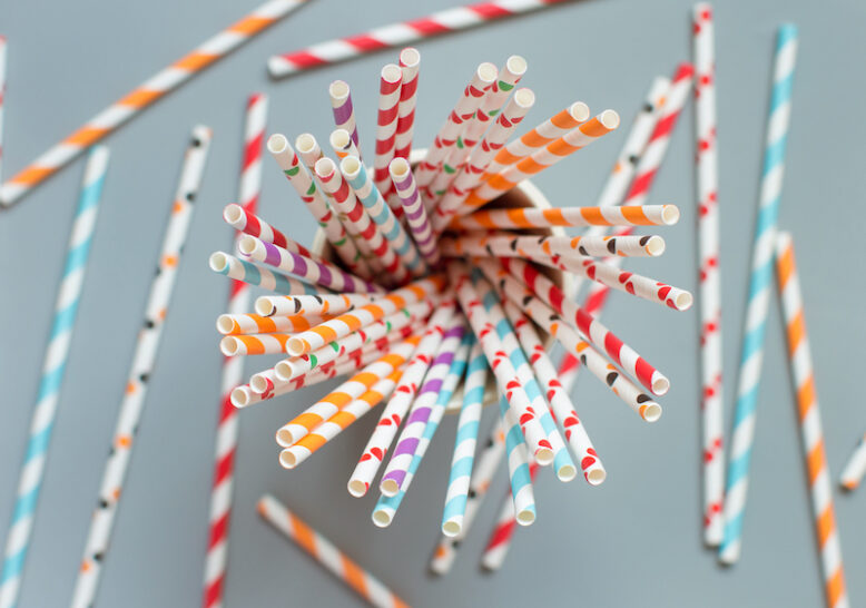 Striped and dotted paper drinking straws in a glass on grey background top view.