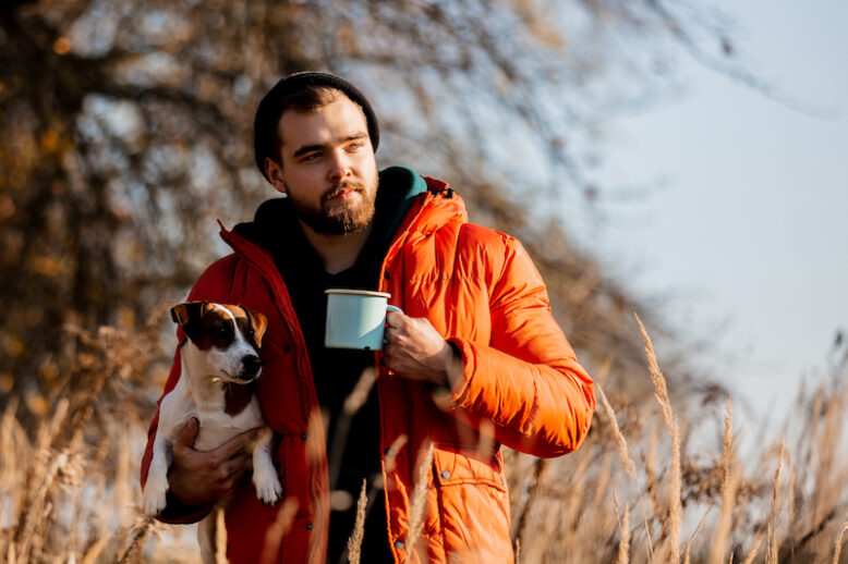 Style man in down jacket with cup and a dog at rural autumn outdoor