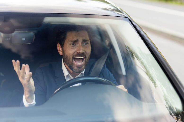 Angry male car driver yells at other drivers and pedestrians who obstruct traffic, mature adult businessman in a business suit is late for a business meeting in a car.